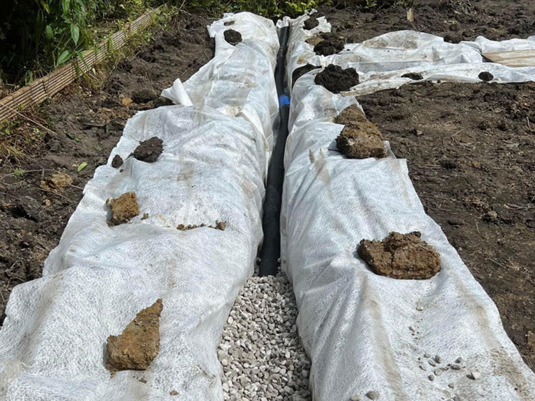 Surface water drainage trench with a perforated land drain bedded in gravel and wrapped in geotextile membrane